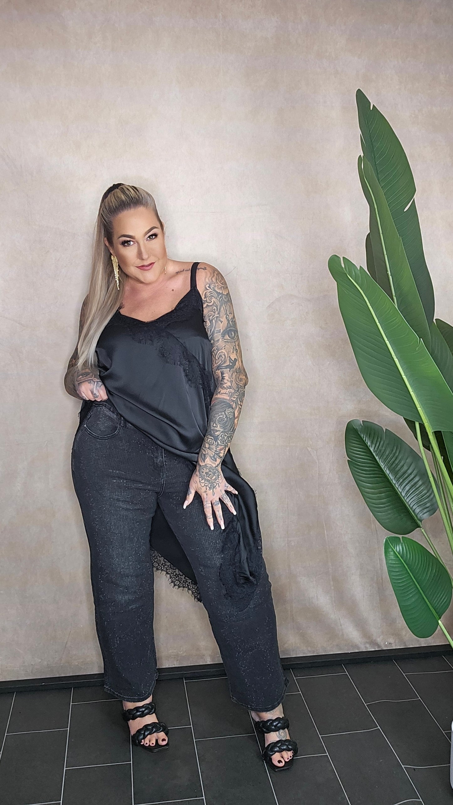 Frau in schwarzem Satin-Spitzen-Top mit Statement-Ohrringen - Frontansicht